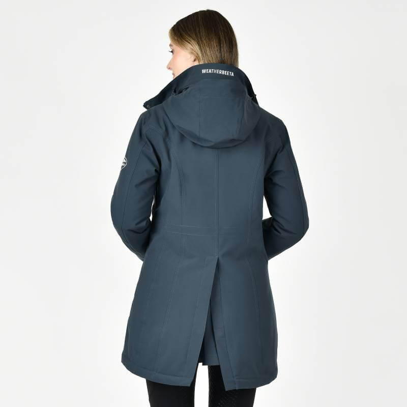 Woman in a pine Weatherbeeta Kyla Waterproof Jacket, facing away with hands in pockets.