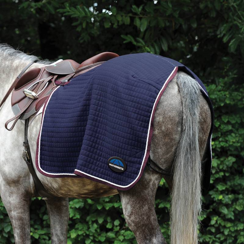 A grey horse with a navy saddle pad, brown saddle, and a Weatherbeeta Thermocell fleece sheet.