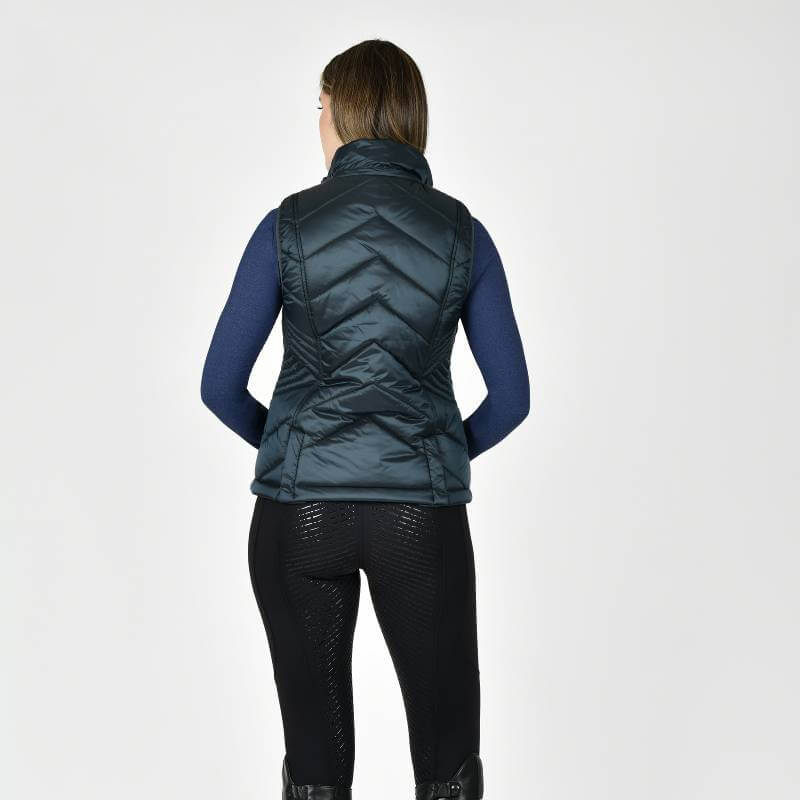 Woman facing away, wearing a Weatherbeeta Presley Puffer Vest Pine and black leggings on white.