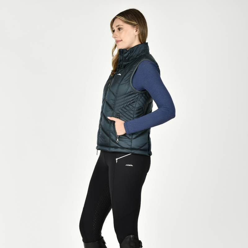 Woman wears a Weatherbeeta Presley Puffer Vest Pine and leggings, standing sideways on white.