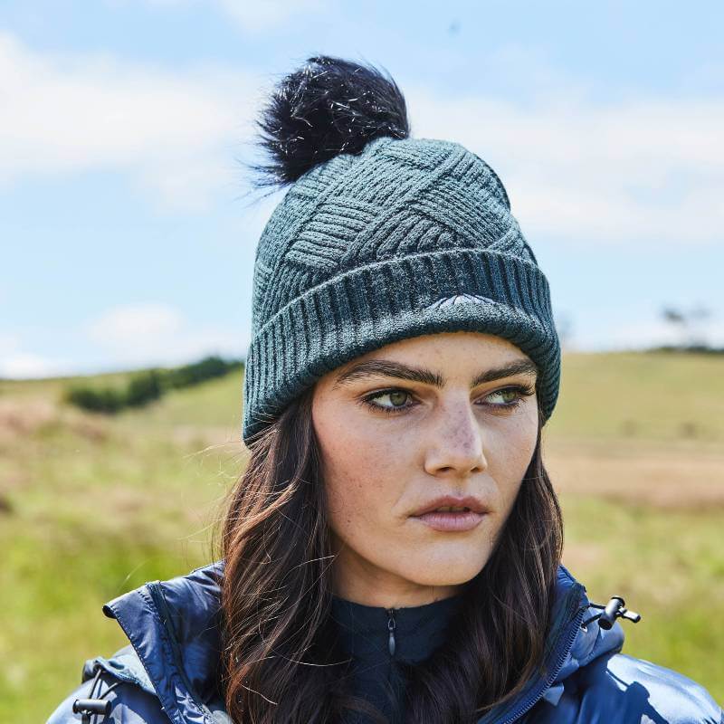 Woman outdoors in a Weatherbeeta Beanie Pine, dark jacket, grassy field in the background.