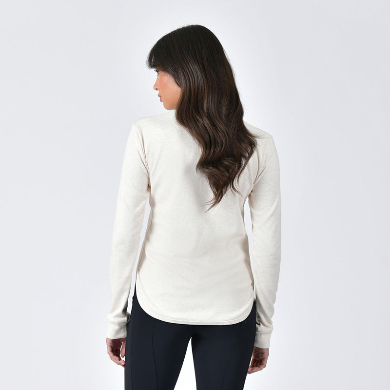 Woman wears Weatherbeeta London Layer Top in light cream marle with black leggings, hand on hip.