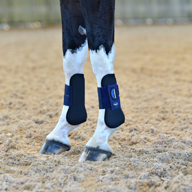 Weatherbeeta Tough-Tec Prime Open Front Boots Black/Navy protect horse legs on sandy ground.