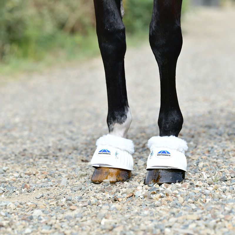 A horse in Weatherbeeta Tough-Tec Prime Fleece Trim Rubber Bell Boots stands on gravel.