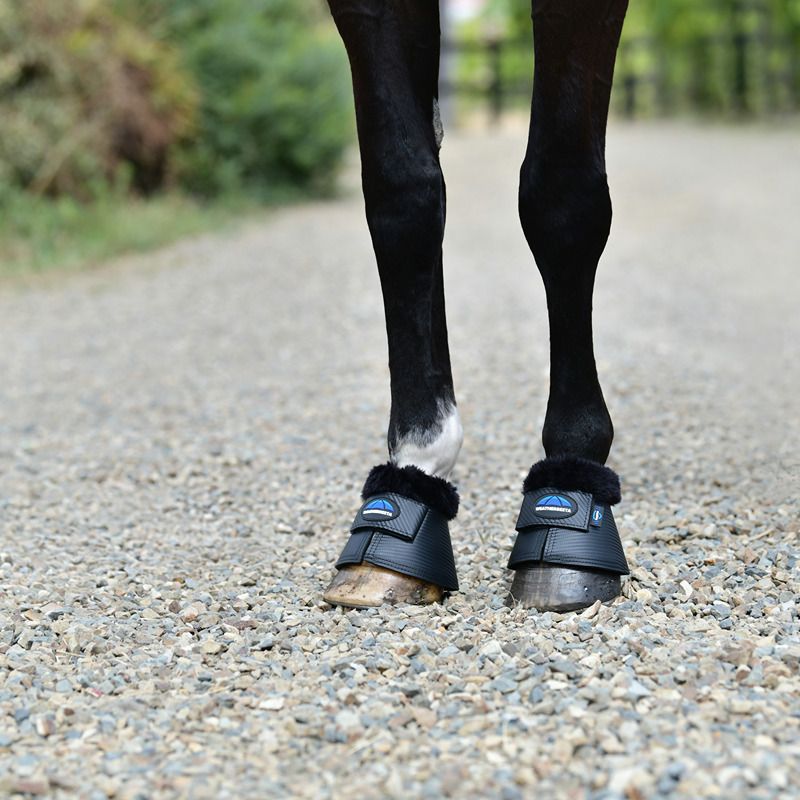 A horse in Weatherbeeta Tough-Tec Fleece Trim Bell Boots Black stands on a gravel path.