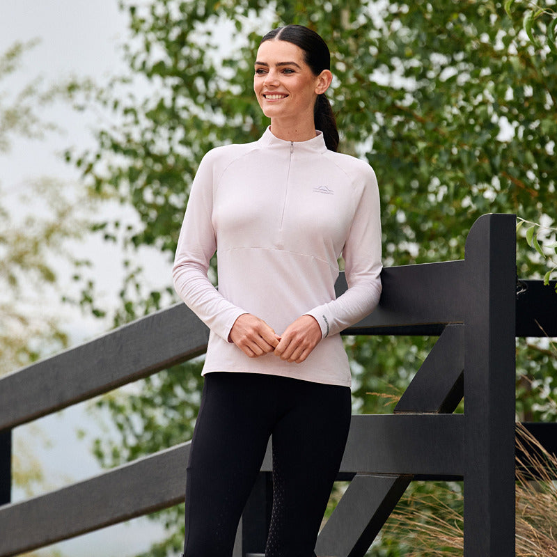 Woman in Weatherbeeta Bamboo Lavender Mist base layer stands, smiling by a black fence.