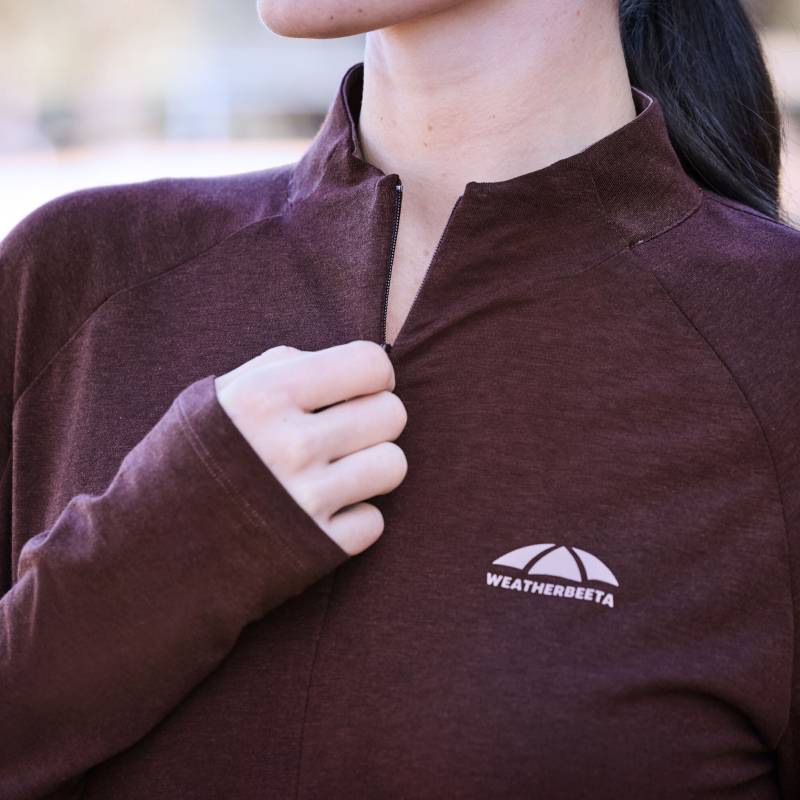Person zipping up a Weatherbeeta Bamboo Long Sleeve Base Layer Mulberry, logo on chest.