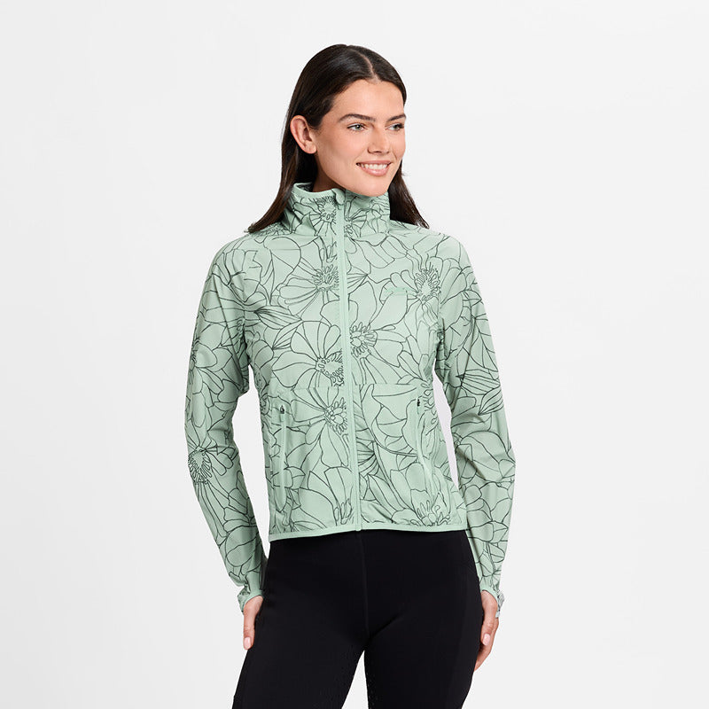 Woman smiles in Weatherbeeta Lightweight UV Jacket Soft Sage/In Bloom and black leggings, hands on hips.