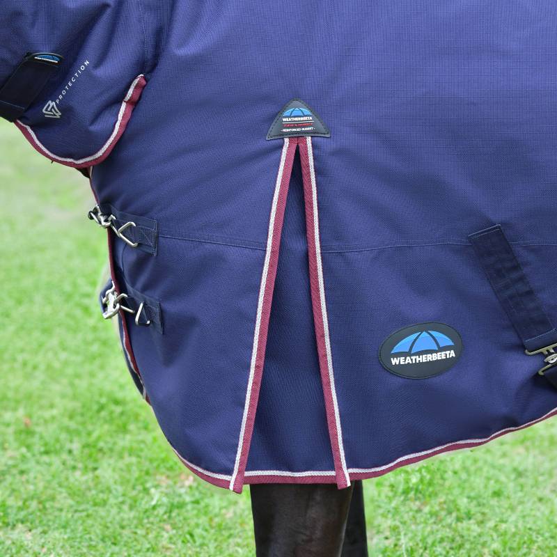 Horse in a Weatherbeeta navy/burgundy 220g turnout rug stands on grass.