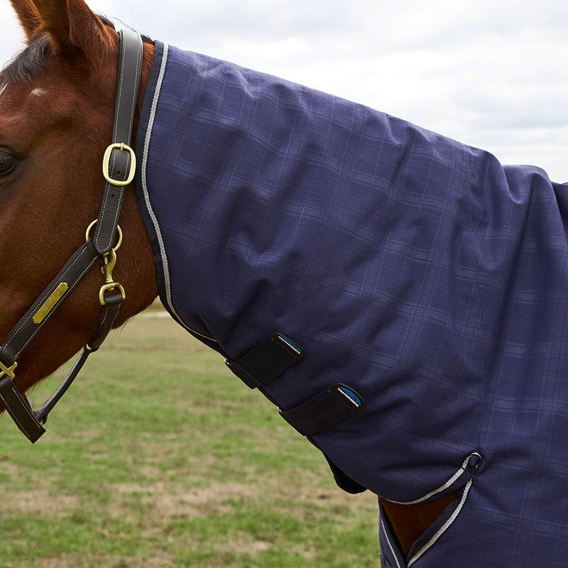 A horse wears a Weatherbeeta Comfitec Prelim Combo Navy Plaid Turnout Rug on the grass.