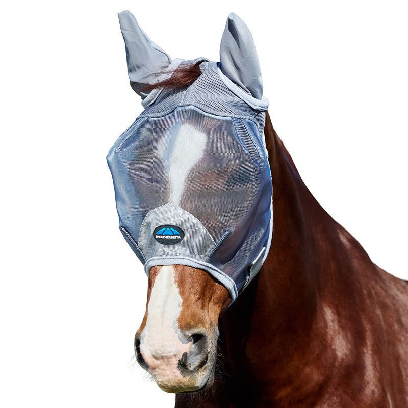 A horse in a Weatherbeeta mesh fly mask with ears, grey, stands outdoors with trees behind.
