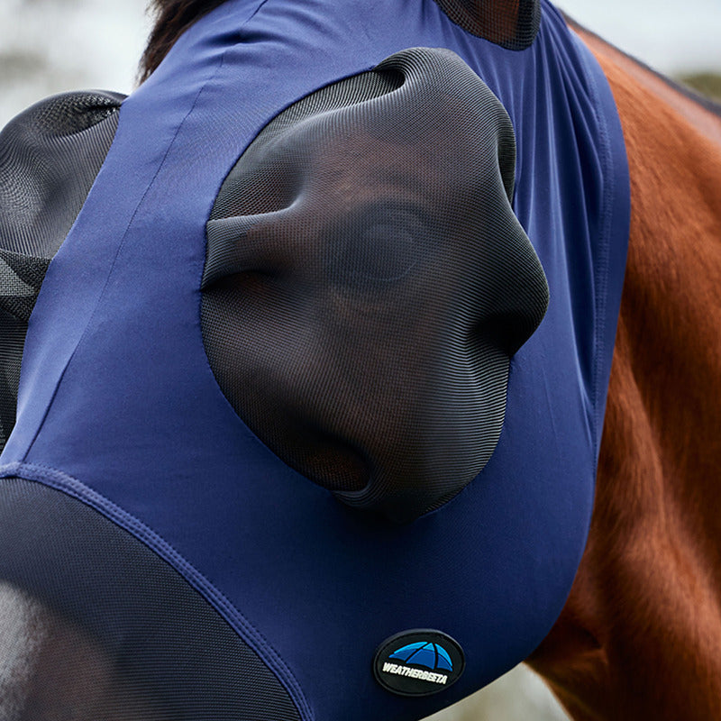 A brown horse outdoors wears a Weatherbeeta navy/black Comfitec Luxe fly mask with ears.
