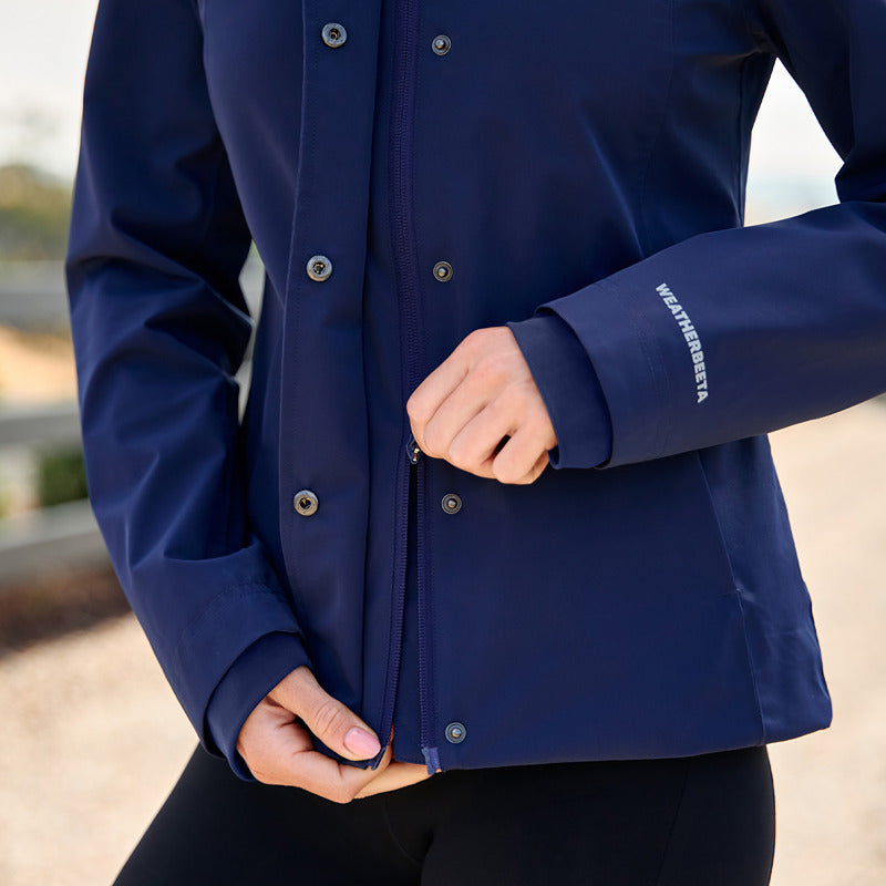 Person zipping up a Weatherbeeta Protect Waterproof Riding Jacket Navy, torso and hands visible.