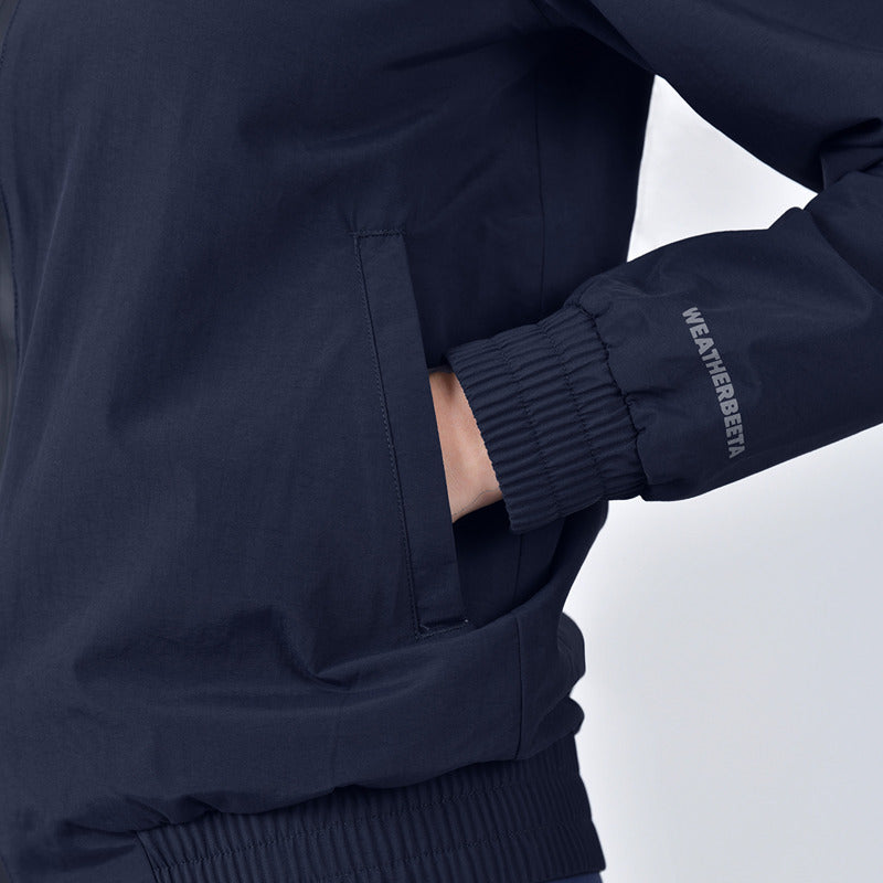 Person wearing a Weatherbeeta Waterproof Team Jacket Navy with hand in pocket, text on sleeve.