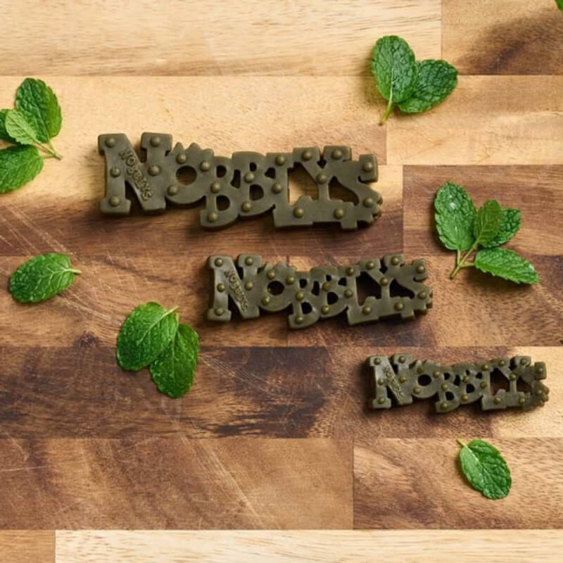 Three Nobblys Mint Dog Chews by Petellos rest on a wooden surface.