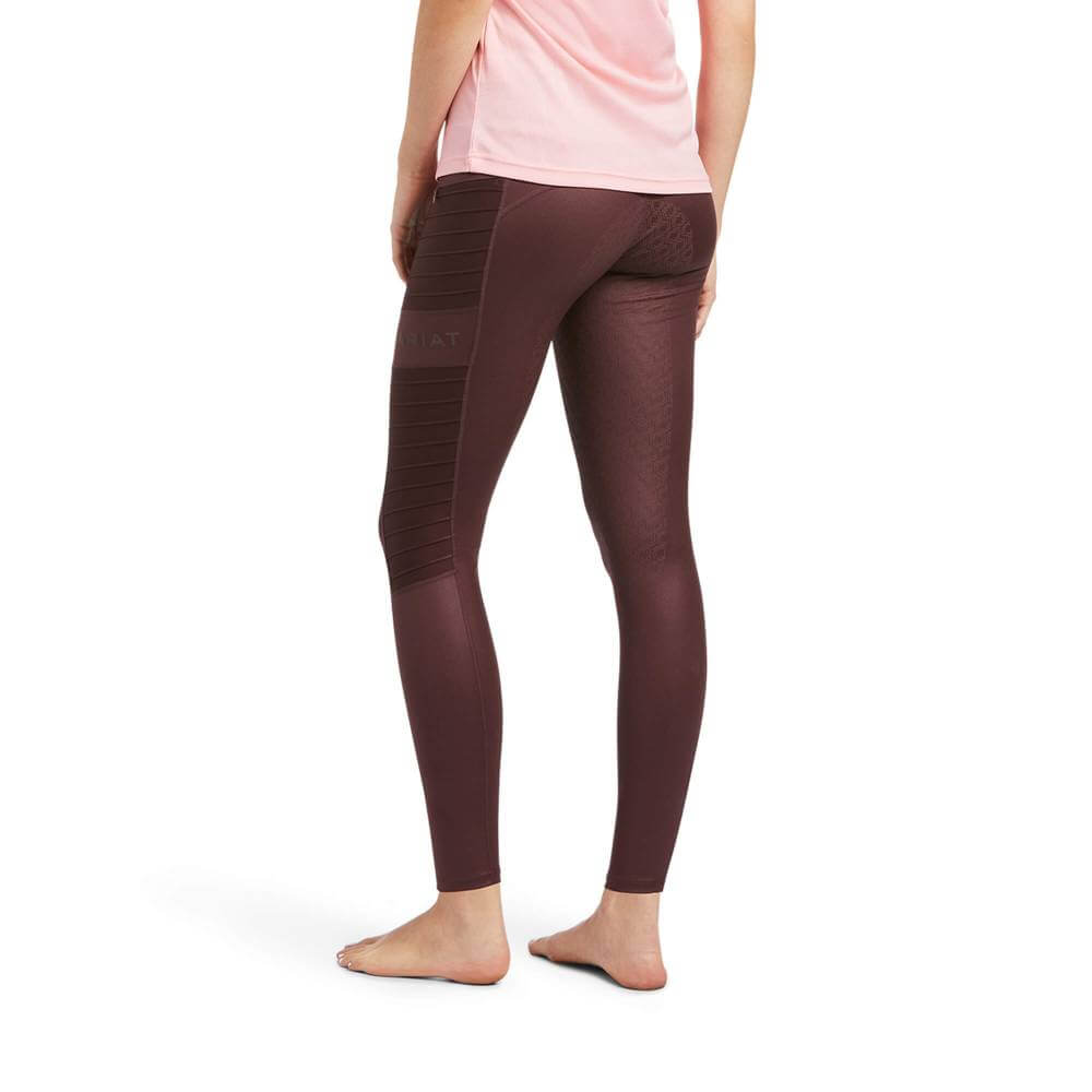 A person in a pink shirt and Ariat EOS Moto Full Seat Tights Deep Mahogany Hide Emboss stands barefoot.