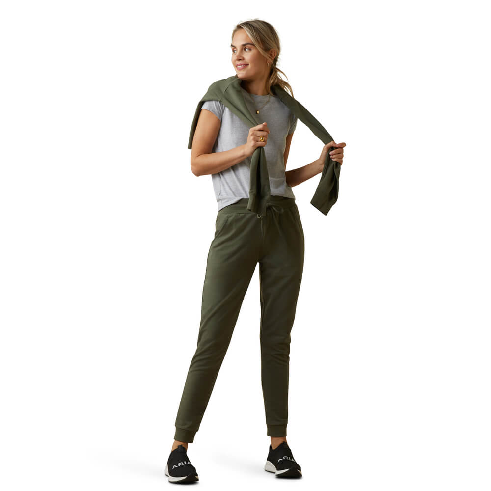 Woman in Ariat Memento Jogger Beetle, gray tee, and sweater tied around her shoulders.