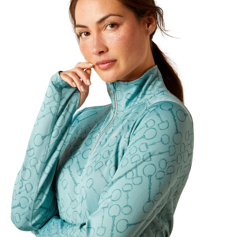 Woman in a light blue Ariat Prophecy 1/4 Zip Arctic and navy pants, hand on her hip.