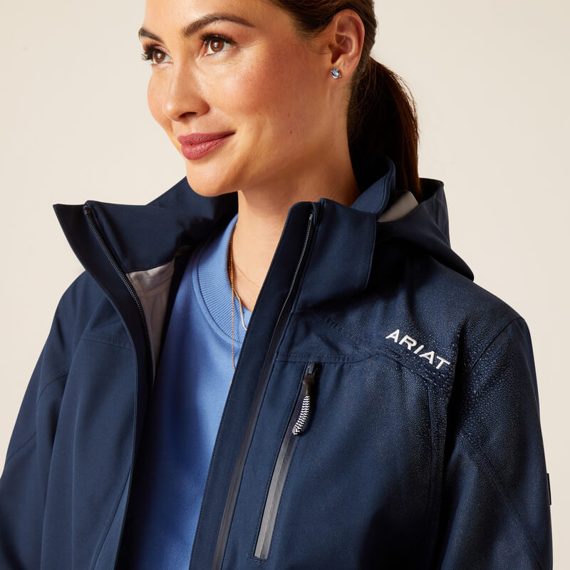 Woman in a navy Ariat Womens Coastal Long H2O Parka, over a light blue shirt, looking aside.