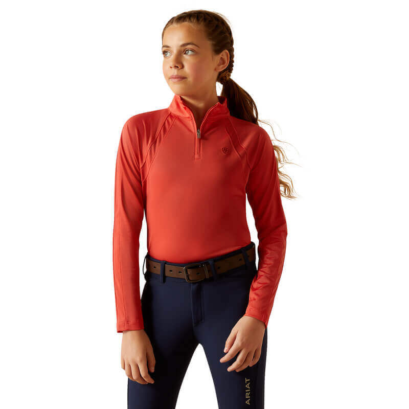 Girl in an Ariat Youth Sunstopper 3.0 Baselayer Baked Apple, blue pants, looking sideways.