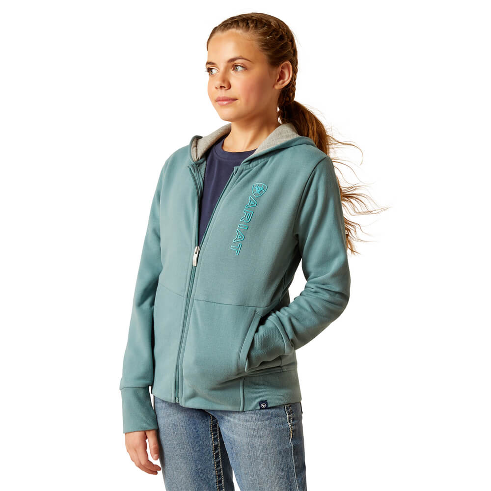 Young woman in Ariat Youth Team Logo Hoodie North Atlantic, hands in pockets, looking aside.