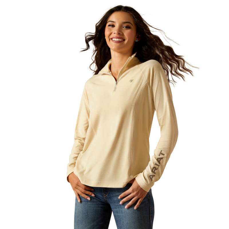 Smiling woman in Ariat Laguna 2.0 ¼ Zip Top Summer Sand and jeans, Ariat on her left sleeve.