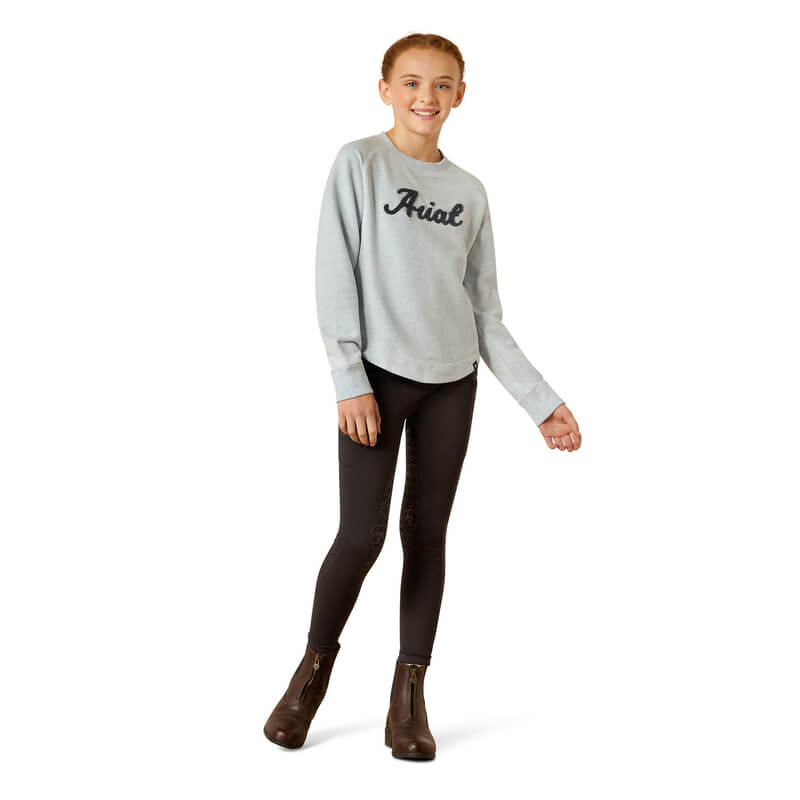 Smiling girl in Ariat Youth Benicia Sweatshirt Cerulean Heather, black leggings, brown boots.