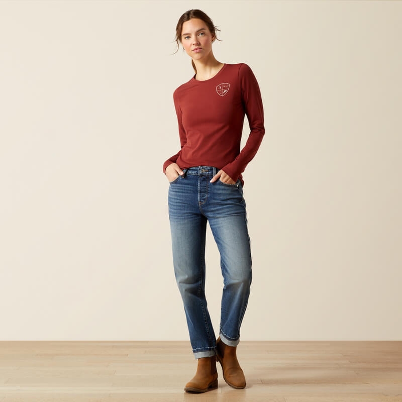 Woman in an Ariat EQ Icons Madder Brown long sleeve tee, jeans, and brown boots with hands in pockets.