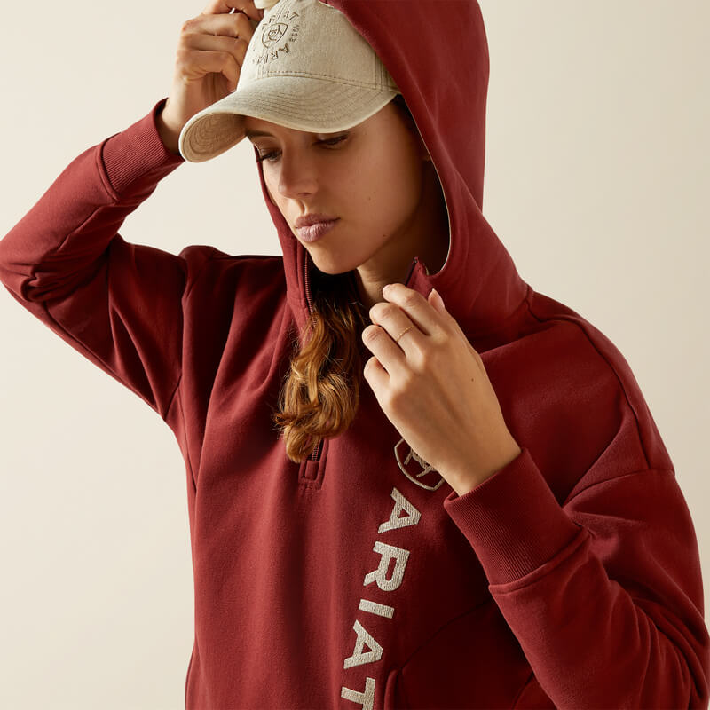Woman in Ariat Womens Rabere 2.0 Hoodie Madder Brown, blue jeans, and a beige cap.
