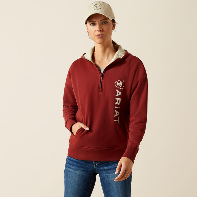 Woman in Ariat Womens Rabere 2.0 Hoodie Madder Brown, blue jeans, and a beige cap.