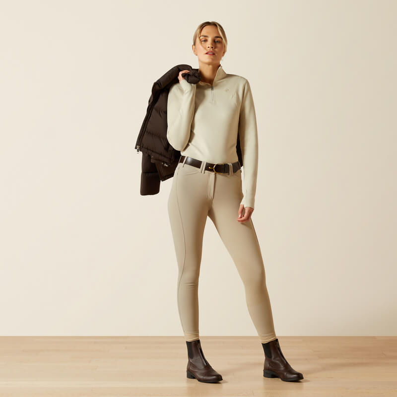 Woman in beige breeches, Ariat Womens Lucent 1/4 Zip Baselayer Pelican, dark boots, jacket draped.