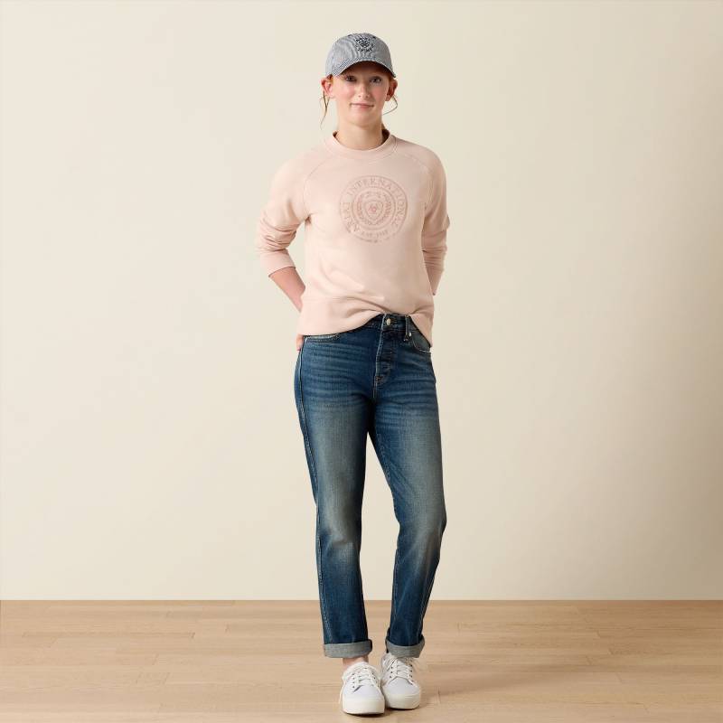 In an Ariat Youth Martine Sweatshirt Sepia Rose, jeans, sneakers, and a cap on plain backdrop.