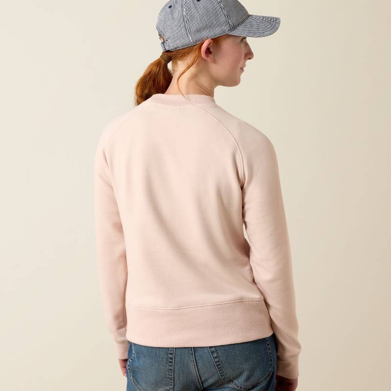 In an Ariat Youth Martine Sweatshirt Sepia Rose, blue jeans, and a striped cap, facing away.
