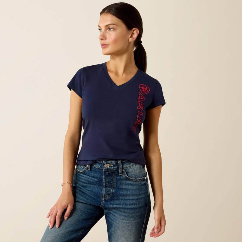 Woman in an Ariat Womens Vertical Logo SS T-Shirt Navy/Red stands against a light background.
