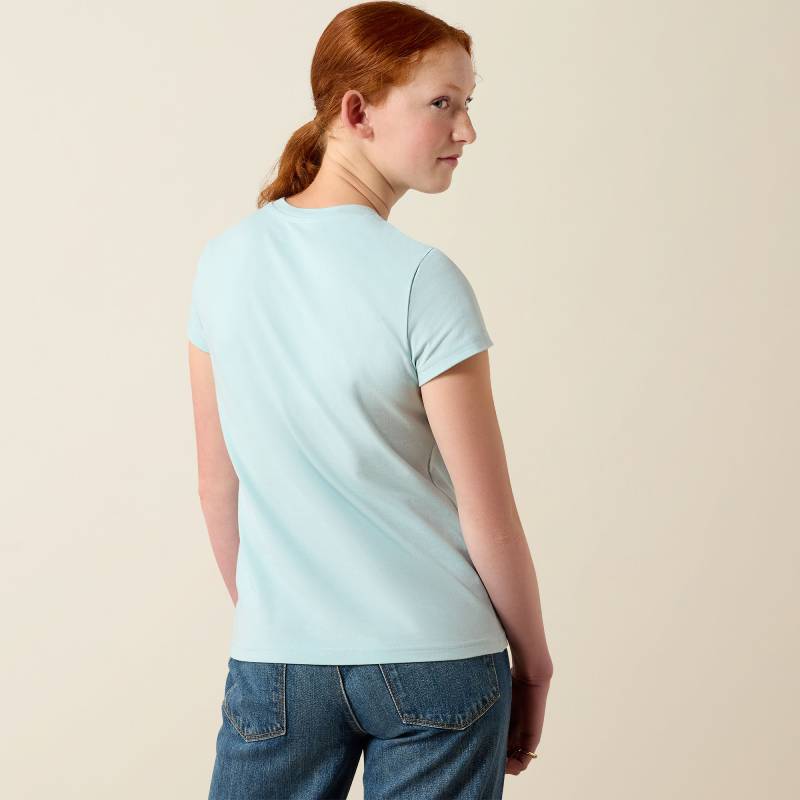 Woman with red ponytail wears Ariat Youth Vertical Logo T-Shirt Starlight Blue, facing back.