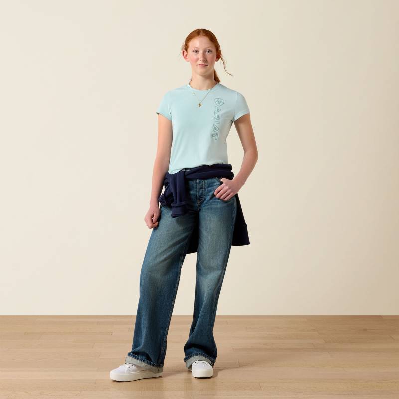 Youth wears Ariat Youth Vertical Logo T-Shirt in Starlight Blue/Blue Surf, standing on wood floor.