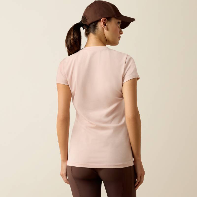 Woman in Ariat Vertical Logo SS T-Shirt Sepia Rose and brown cap, facing away, plain background.