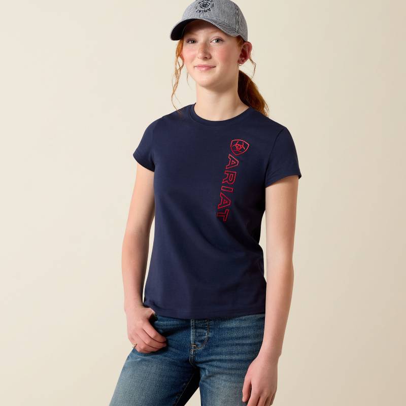 Teen girl in Ariat Youth Vertical Logo SS T-Shirt Navy/Red, hand in pocket, smiling brightly.