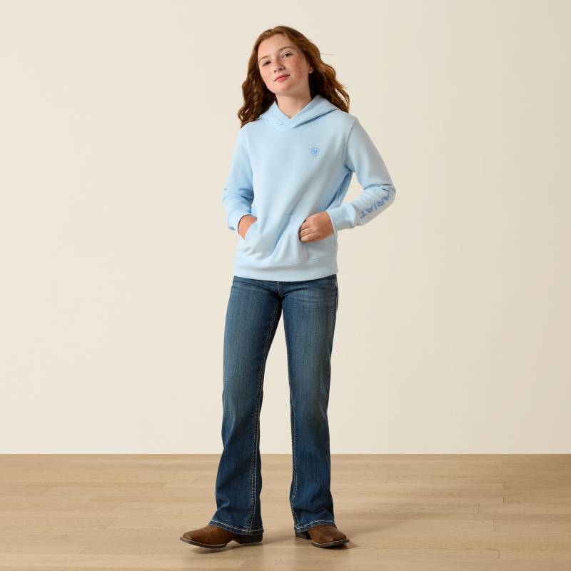 Girl in Ariat Girls 2.0 Hoodie Nantucket Breeze, jeans and boots on wood floor near beige wall.
