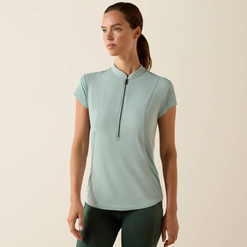 Woman in Ariat Breathe 1/2 Zip Cap Sleeve Baselayer Blue Surf, dark leggings, beige backdrop.