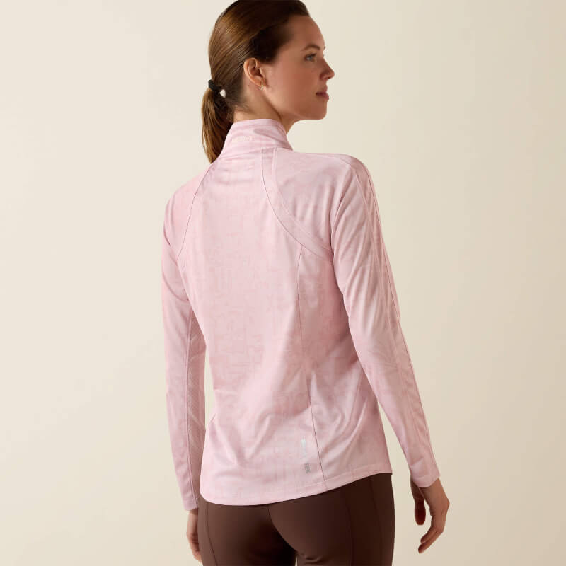 Woman in a sepia rose Ariat Womens Sunstopper 3.0 Baselayer, brown pants, neutral background.