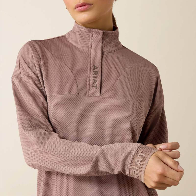 Woman in Ariat Breathe 1/2 Zip Pullover Antler, matching hat, and brown leggings stands confidently.