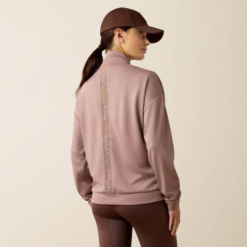 Woman in mauve Ariat Breathe 1/2 Zip Pullover Antler, cap on, Ariat logo visible on back.