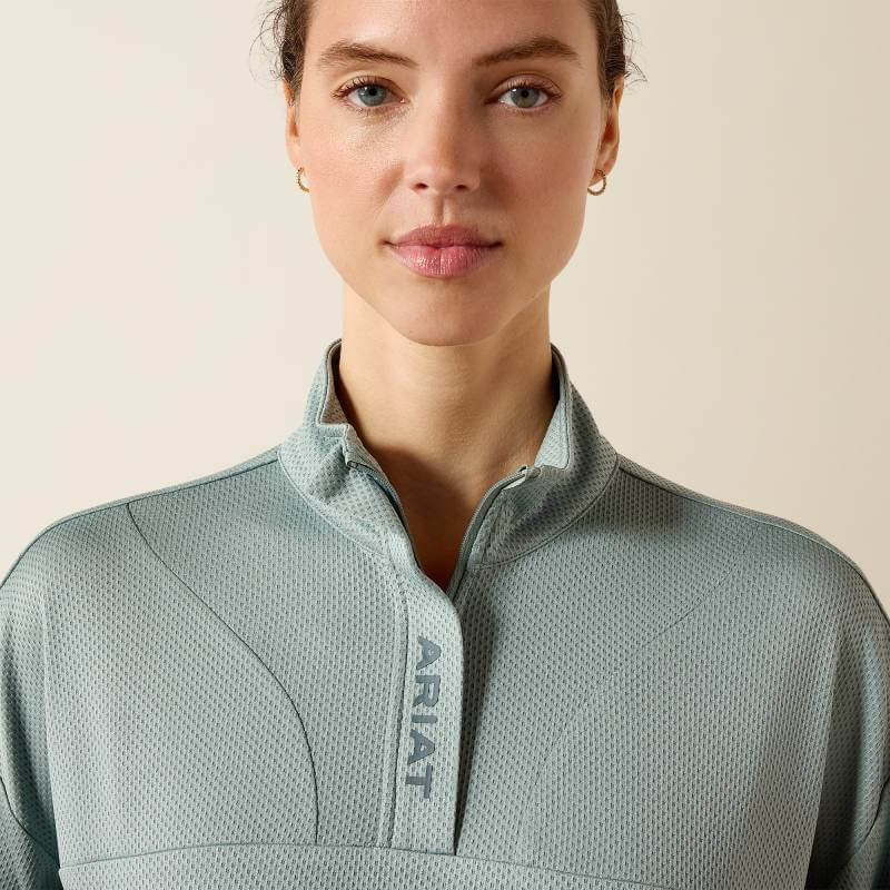 Woman in Ariat Breathe 1/2 Zip Pullover, Chinois Green, stands against a beige background.