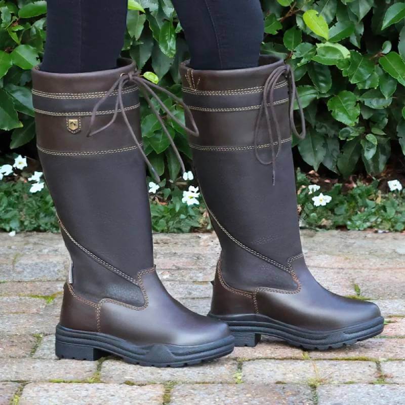 Hy Equestrian Hy Tideswell Country Boots Childs Brown, worn on a stone path by green bushes.