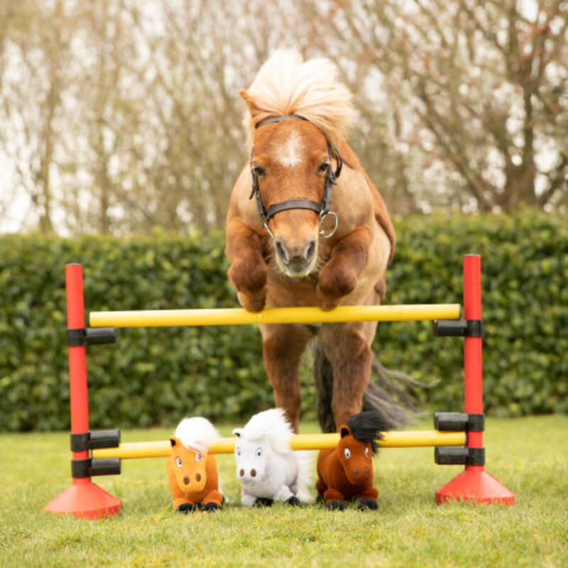 Thelwell Ponies Fiona & Merrylegs plush jumps a hurdle with three toy horses below.