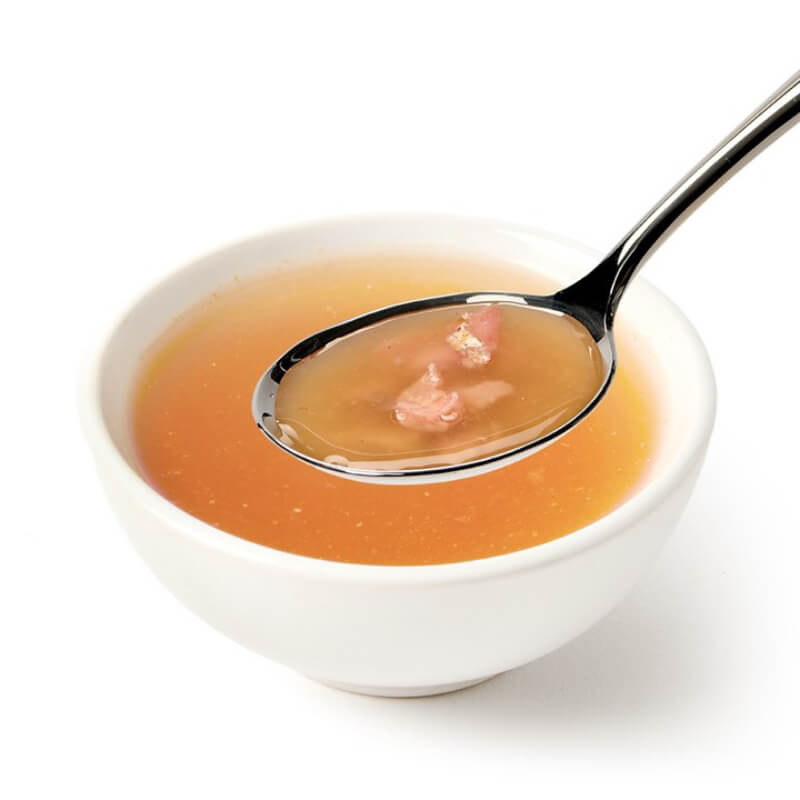A spoon with broth and protein above a bowl of Canagan Chicken Cat Soup 140g.