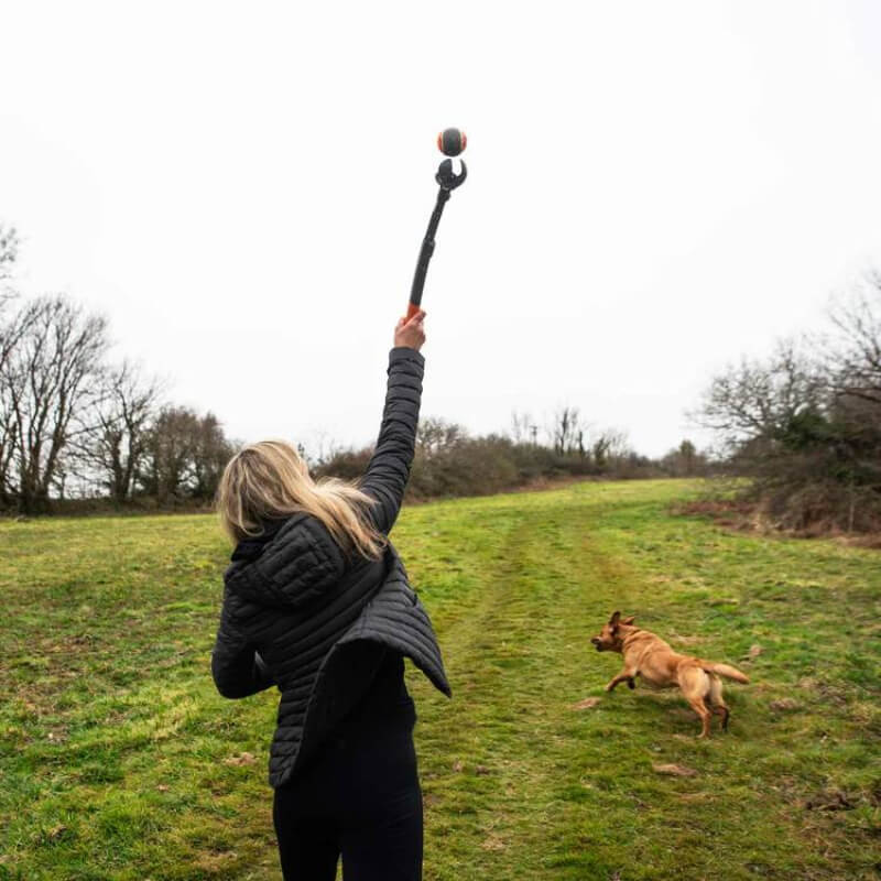Mountain Paws Dog Ball Launcher Adjustable holds a tennis ball, with orange and black design.