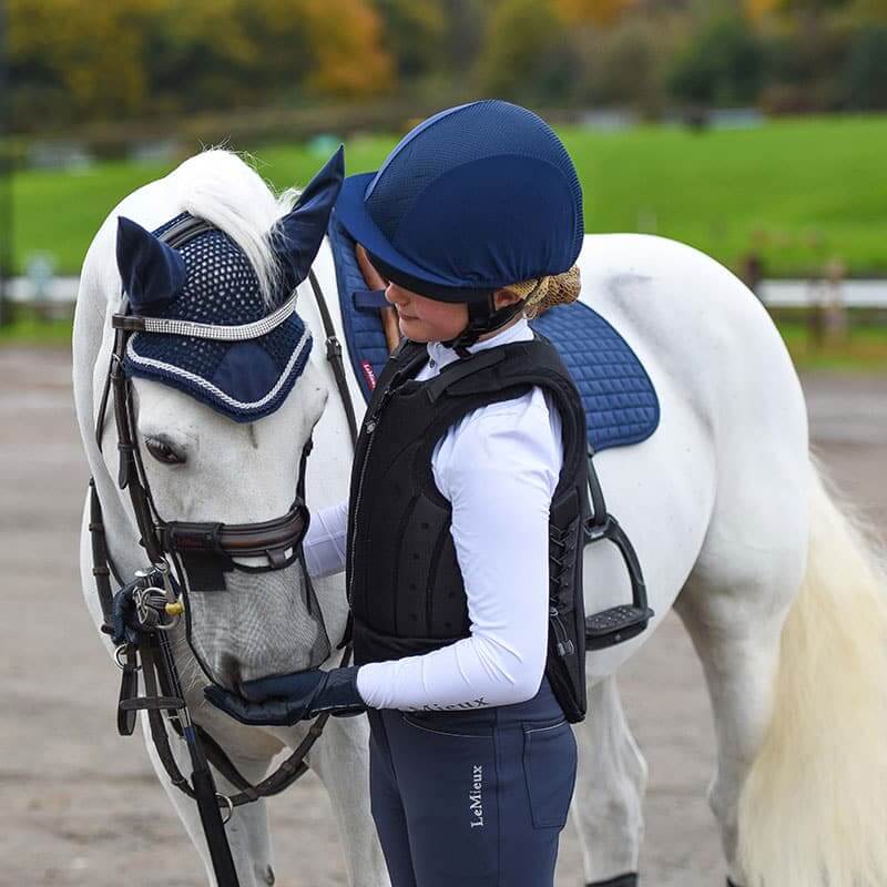 A young rider in a Charles Owen Kontor Black Childs helmet gently pets a white horse.