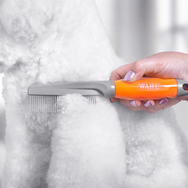 A hand grooms a fluffy white dog with a Wahl Grooming Comb Orange Gel Handle.